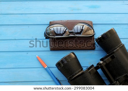 Preparation for travel - wallet, binoculars, sunglasses and pen - on blue wooden table