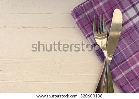 Plaid tablecloth, knife and fork on wood textured background