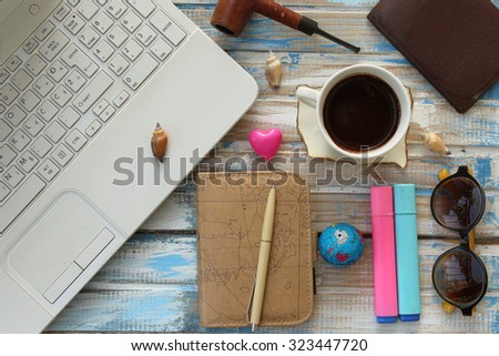 Top view of office table top with laptop computer, coffee cup, notebook planner, pens, sunglasses, smoking pipe, wallet and decoration