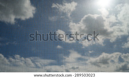 Closeup of mosquito wire screen with sun ray on blue sky and white clouds in background