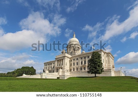 Wide-angle view of the front of the Rhode Island state capitol building as it sits on Capitol Hill in Providence with bright blue sky and white clouds in the background