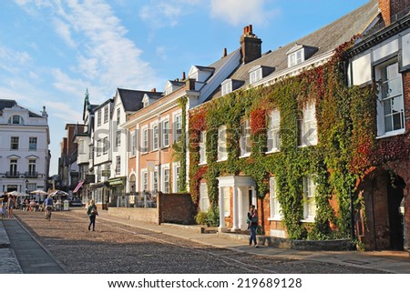 EXETER, UK - SEPTEMBER 12 2014: Pedestrians walk by businesses and residences on Cathedral Close and Cathedral Yard. This is a popular area for tourists and residents to relax near Exeter Cathedral.