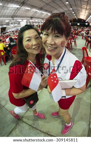 SINGAPORE - AUGUST 8 : Fisheye shot of two female with SG50 tattoo on faces, hold mini national flags with pride and joy at Pasir Ris - Punggol SG50 National Day dinner event on Aug 8, 2015, Singapore