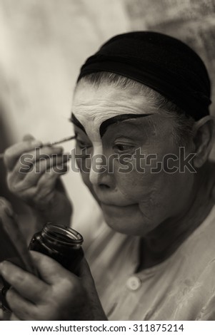 SINGAPORE - AUG 20: Dark sepia version of an elderly Chinese Teochew opera singer doing her own makeup on Aug 20, 2015 in SINGAPORE.