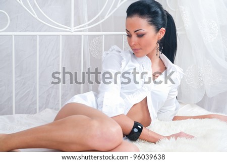 Seductive young woman lying on a bed in white blouse with legs naked