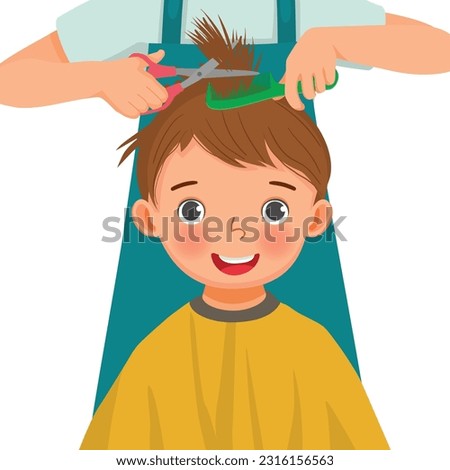 Cute little boy getting hair cut by hair dresser in the hair salon