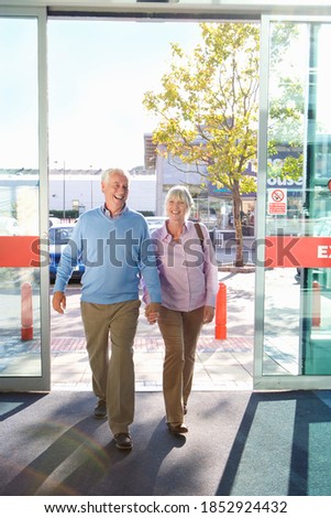 Smiling senior couple walking hand in hand into an electronics appliances store through glass doors