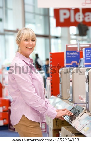 Senior woman in the electronics store buying a new computer and typing on a keyboard while smiling at the camera