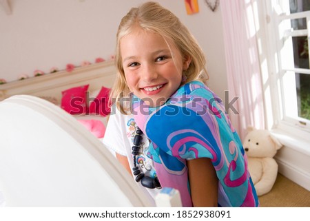 Horizontal waist up portrait of a girl playing dress-up in bedroom in front of a mirror smiles at the camera.