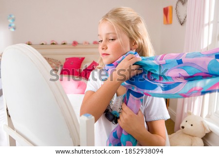 Horizontal waist up portrait of a girl playing dress-up in bedroom in front of a mirror.