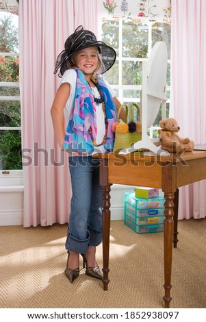 Vertical portrait of a girl playing dress-up in the bedroom smiles at the camera.