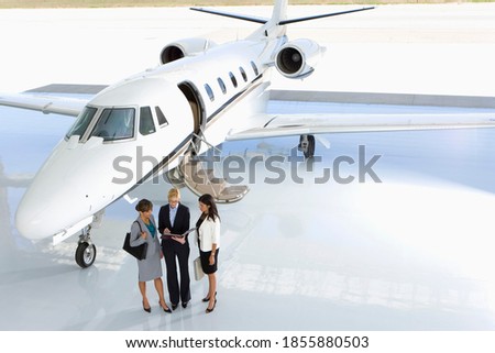 Horizontal shot of three businesswomen posing in front of a private jet on the runway.