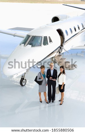 Elevated view of three businesswomen posing in front of a private jet on the runway.