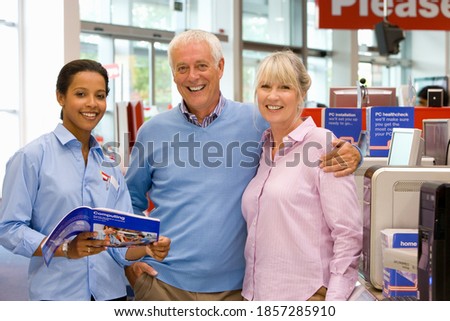 A young saleswoman holding a catalog is helping a senior couple with the purchase of a new personal computer