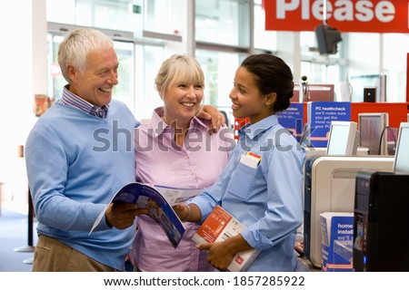 A young saleswoman is helping a senior couple with the purchase of a new personal computer and pointing at something in a brochure