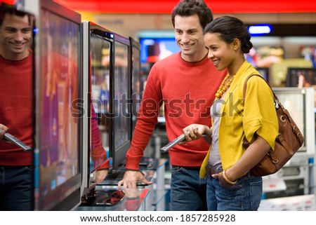 Young mixed race couple standing in the middle of an electronics appliances store and shopping for a new television