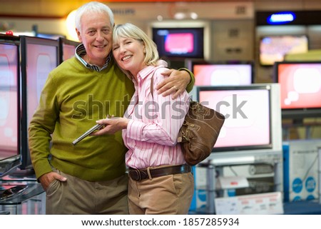 Senior couple hugging in the middle of an electronics appliances store and shopping for a new television