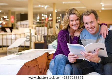 Middle-aged woman hugging her husband while checking out a catalog in the furniture shop and both are smiling at the camera