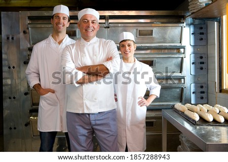 Team of bakers standing next to a tray of baguettes waiting to be baked in the oven in the bakery