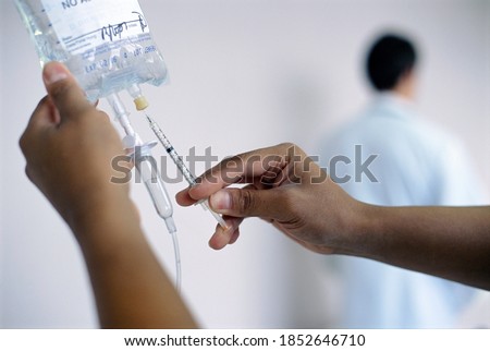 Close up of nurse?s hands while setting up an intravenous saline drip with doctor standing in the background wearing a lab coat