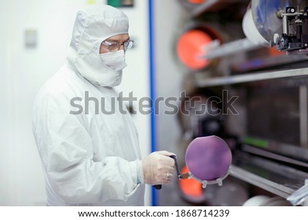 An Engineer in lab suit carefully holding the silicon wafer in a clean processing room