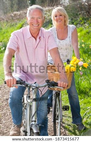 Vertical shot of a senior couple with their bicycles on a sunny day smile at the camera with the man in front.