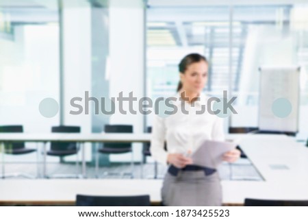 A defocused medium shot of a businesswoman holding paperwork in a conference room.