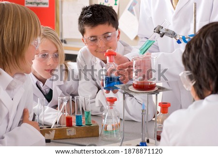 Curious students in lab coats and safety goggles closely watching the ...