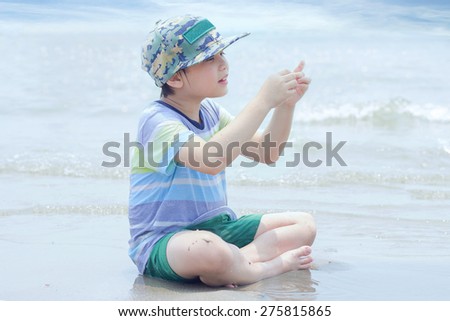 Little asian boy sitting on the sand. Sea and seashore as background.