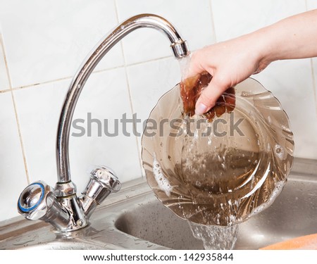 woman hands rinsing dishes under running water in the sink