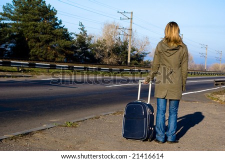 Young smiling woman with suitcase standing at road .
