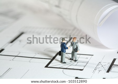 Miniature models of an architect and property owner shaking hands outside the building site of his new house