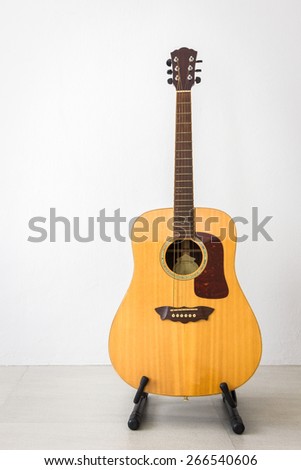 wooden folk guitar stand on the floor with light gray background