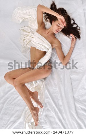 Beautiful naked woman in panties laying on white bed. View from above.
