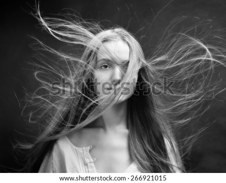 Portrait of the beautiful blonde woman with flying long hair. She is in studio . Monochrome image