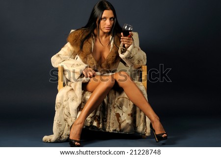 beautiful woman dressed in furs is sitting on the chair and drinking wine