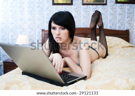 Portrait of the beautiful woman with laptop. She is lying on the bad in underwear.