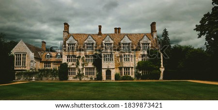 Panoramic, spooky old english manor house with lawn trees. Dramatic cloudy and overcast sky 