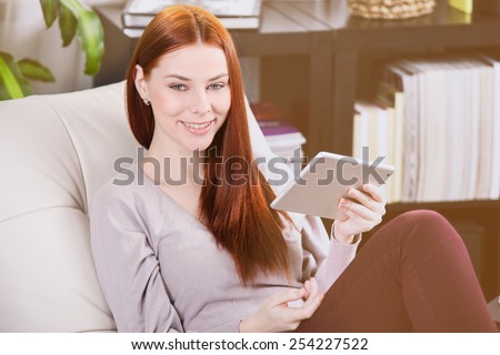 Thin young girl read the tablet on the sofa in the room.