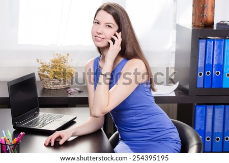 Elegant business woman talking on mobile phone and work on the notebook in the office.