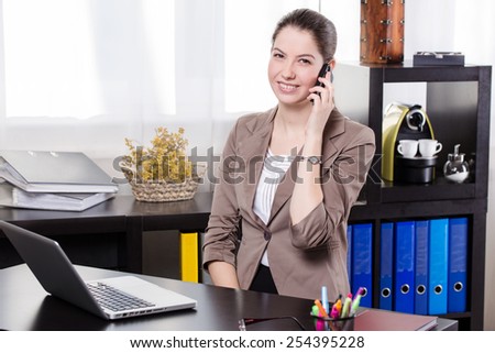 Elegant business woman talking on mobile phone and work on the notebook in the office.