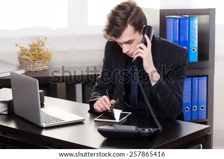 Business man call someone on the landing phone and use the tablet in the office