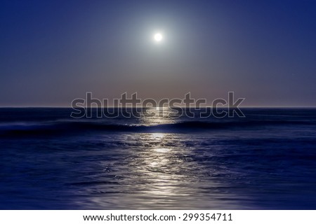 Long exposure, full moon setting, with stars, moonbeam, seafoam, back dropped on a blue sky on Moonstone Beach, along the Big Sur Highway, on the California Central Coast, near Cambria CA.