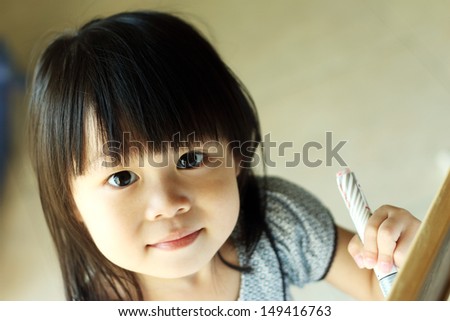 Asian girl looking up at camera while writing on board with pen in hand