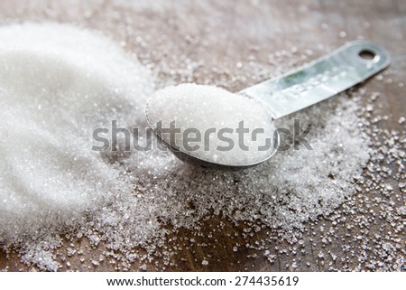 Close-up of granulated sugar in spoon and sugar pile on wooden