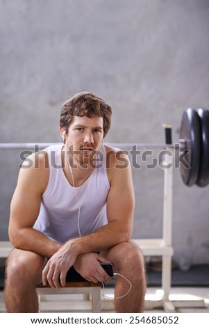 Young man with earphones sitting his private gym ready for a session