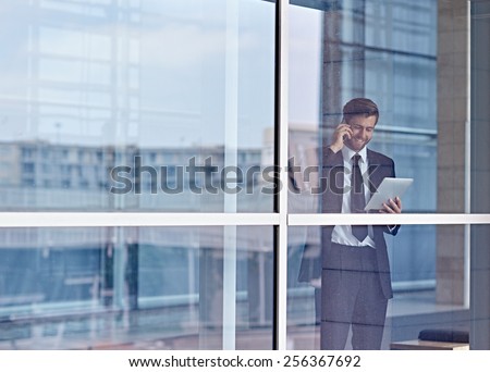 View through a window of a corporate executive talking on his phone and looking at a digital tablet