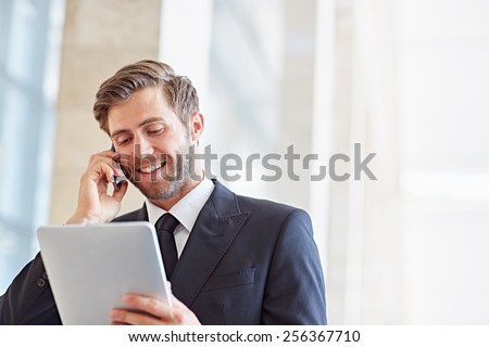 Corporate executive smiling while talking on his phone and looking at a digital tablet