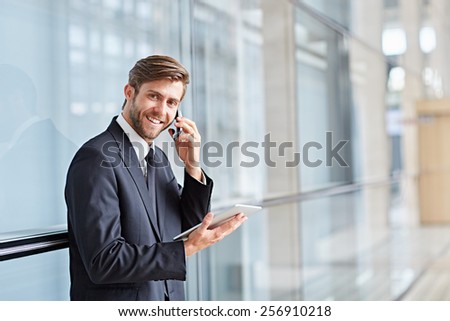 Portrait of a corporate executive smiling while talking on his phone and holding at a digital tablet