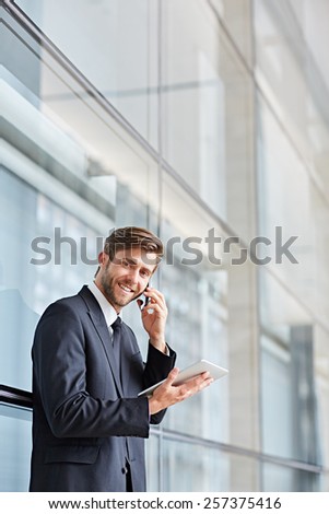 Corporate executive smiling at the camera while talking on his phone and holding at a digital tablet